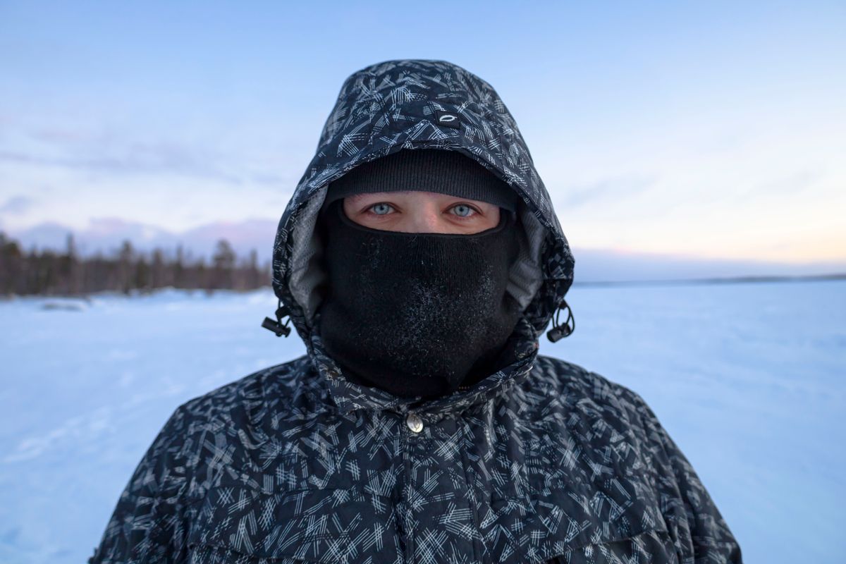 A person bundled up in winter clothing stands on a snowy landscape at dusk.